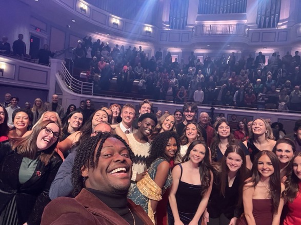 A large group of Songbook Academy alumni pose for a selfie together on stage during an alumni performance.