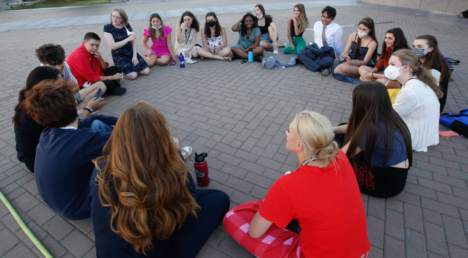 Group of students sitting outside on a brick patio in a circle laughing and smiling