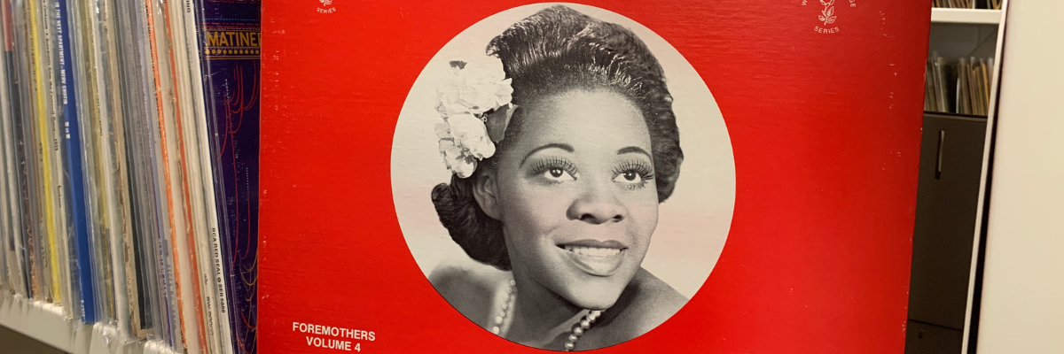 A vinyl album cover with a red background and a photo of Dinah Washington wearing a flower in her hair with finger waves, and pearls.
