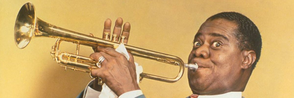 Louis Armstrong looks at the camera mischeviously as he plays his trumpet.