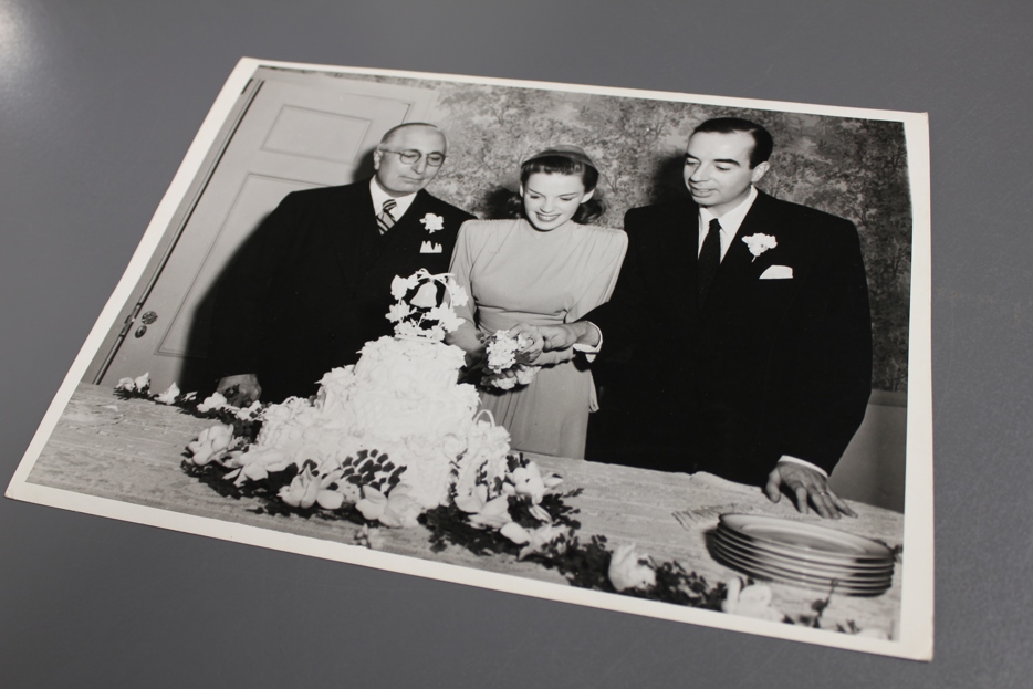 Judy Garland, in a wedding dress, smiles and cuts a cake next to her husband, director Vincente Minnelli.