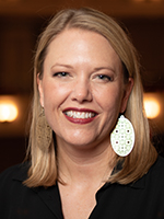 A blonde woman with large earrings smiles for a photo.