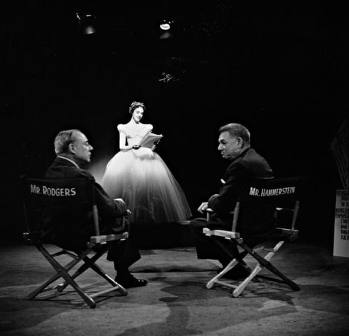 Richard Rodgers and Oscar Hammerstein sit in directors chairs and chat while Julie Andrews sings in the background.
