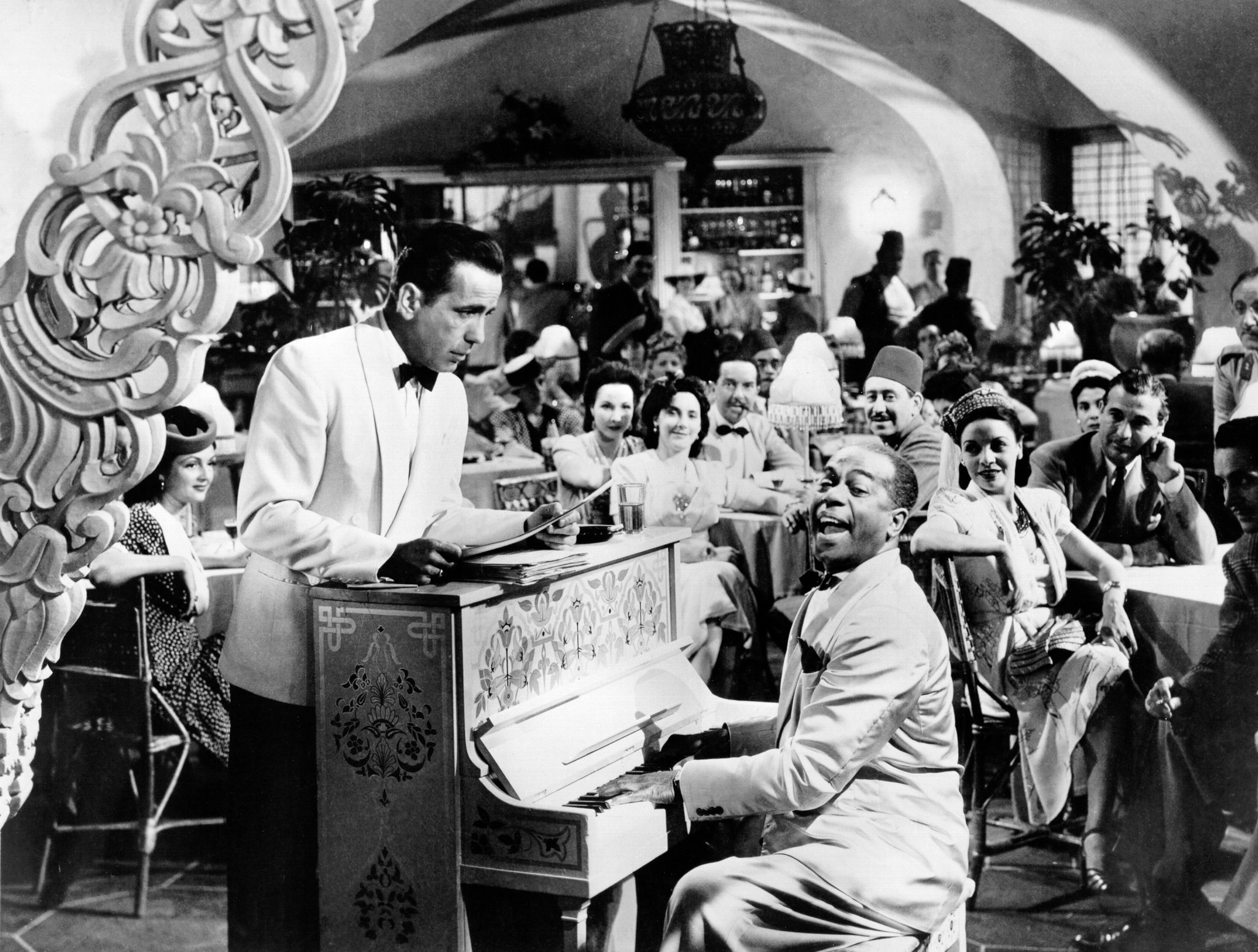 A scene from Casablanca showing Humphrey Bogart listening while Dooley Wilson, as Sam, plays the piano.