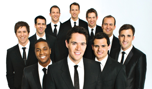 The all-male ensemble of Straight No Chaser pose wearing tuxes and smiles.