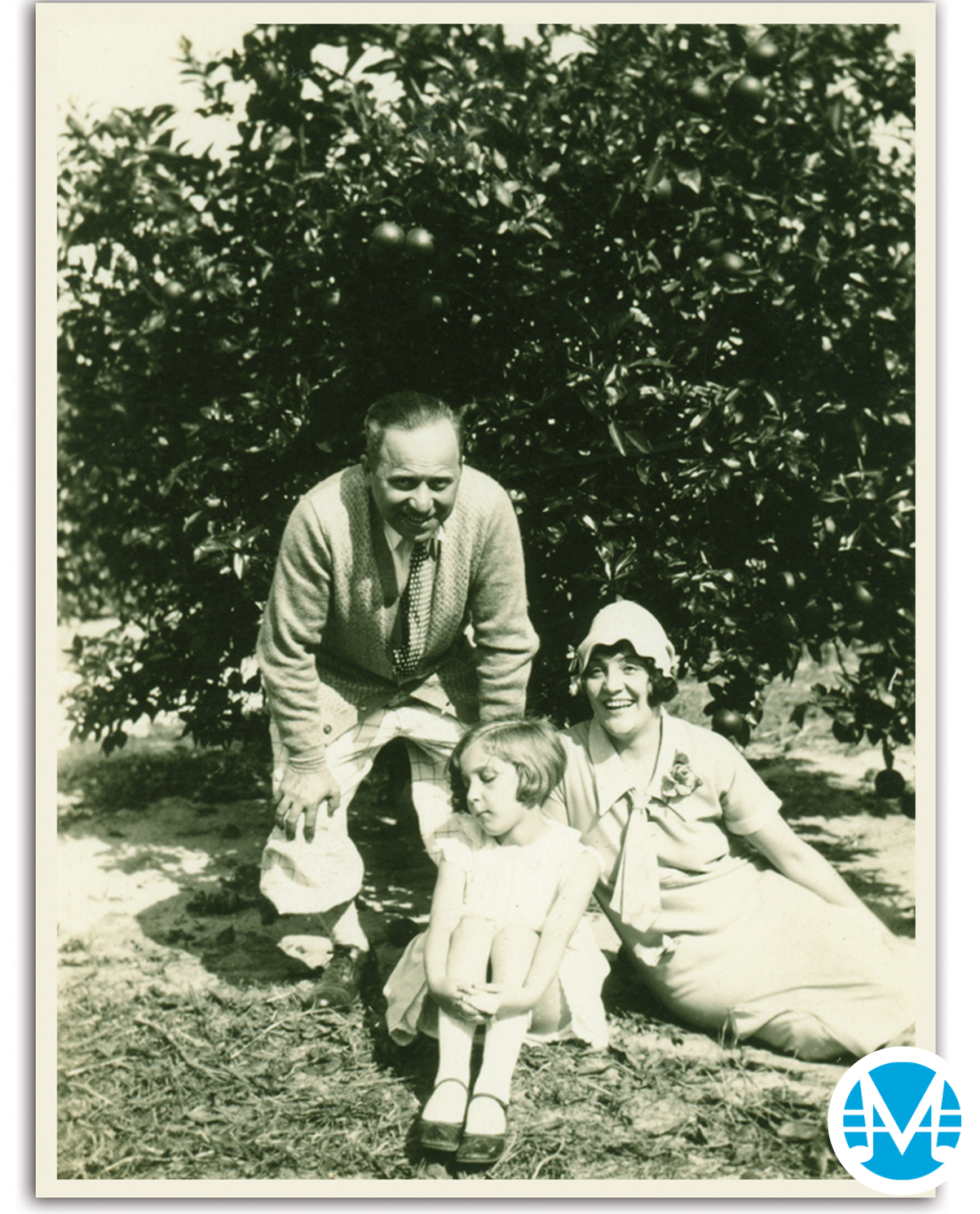 Gus Kahn leans over his wife and daughter and they smile outside.