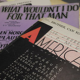 A stack of vintage sheet music shows the song titles "What Wouldn't I Do for That Man" and "Brother, Can You Spare a Dime."