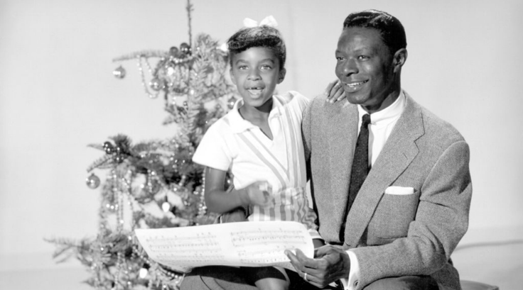 Natalie Cole as a child sits on her father, Nat's lap in front of a Christmas tree.