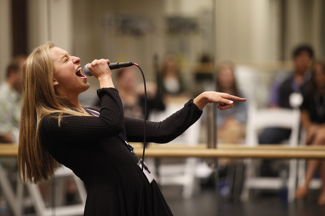 Blonde girl in black leans back to sing in a microphone