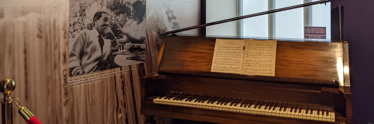 Polished wooden upright piano with sheet music sitting on the ledge and the lid propped open.