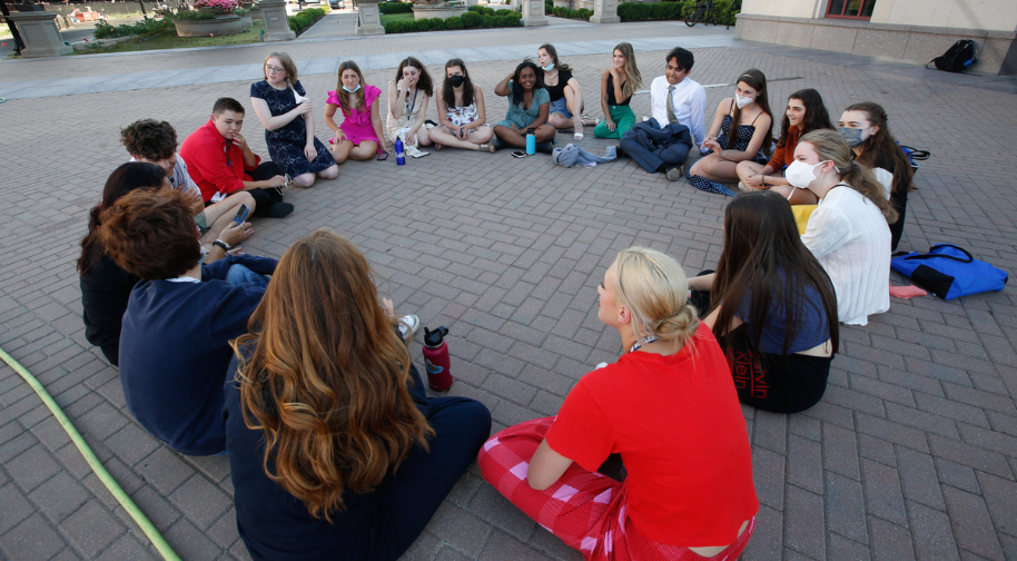 A group of Songbook Academy students sit outside on the ground in a large circle