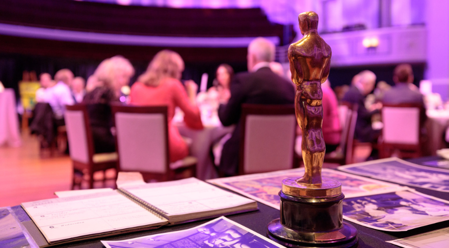 A gold Academy Award statuette sitting on a table of artifacts as attendees eat dinner at an event.