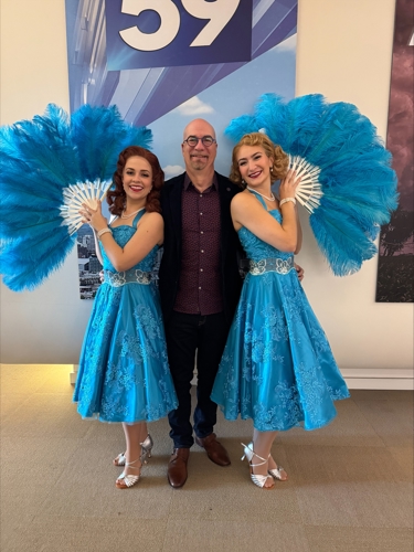 Michael Lasley in a suit jacket and jeans with two actresses playing the Haynes sisters from "White Christmas" dressed up in their blue "Sisters" outfits and fans