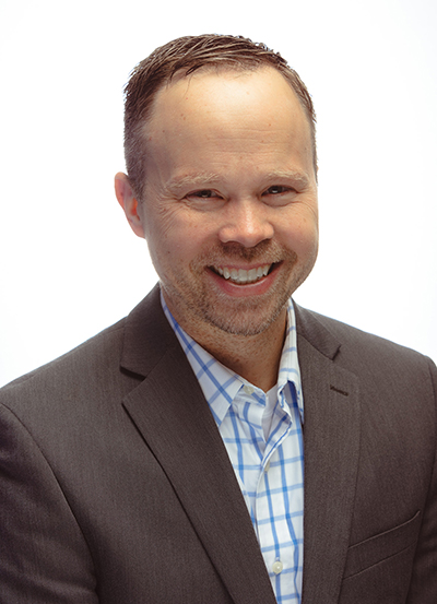 A man with short hair wearing a sportcoat smiles for a photo