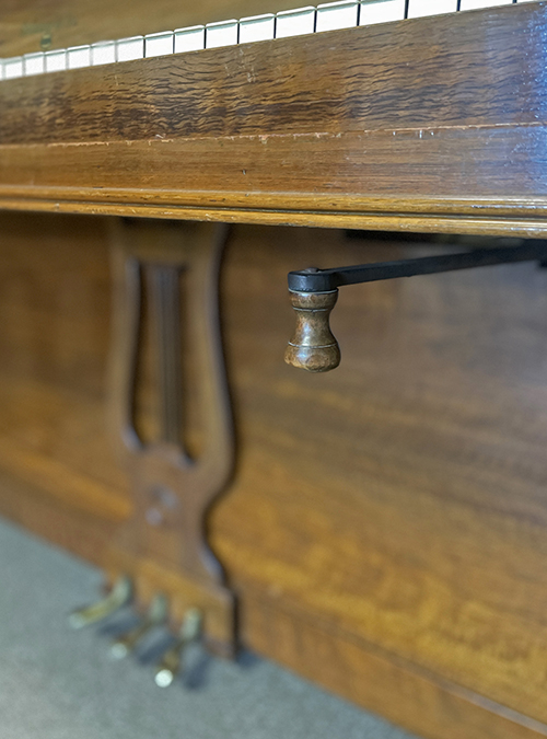 Closeup of an upright piano with a strange lever under the keyboard