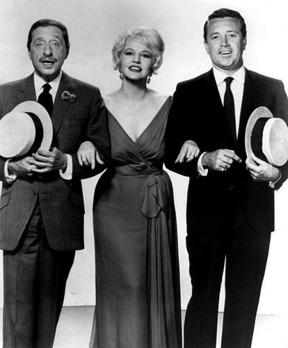 Harold Arlen and Vic Damone are both dressed in suits and hold top hats. They both have their arms linked with the blonde songstress Peggy Lee.
