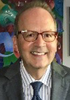 Headshot of a man wearing a gray suit and glasses