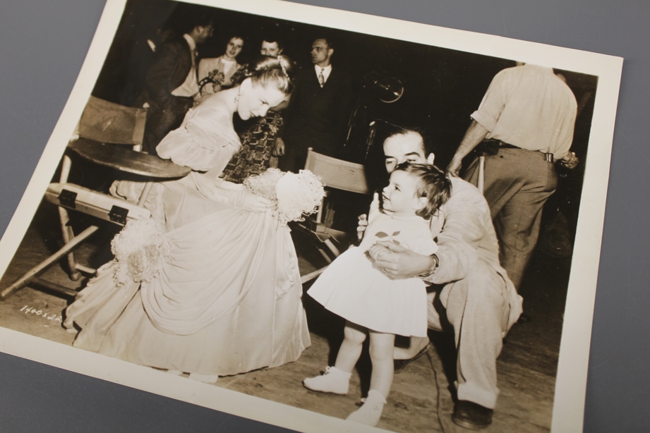 Judy Garland is in a Victorian dress backstage on a movie set. Liza Minnelli as a toddler is held by a kneeling Vincente Minnelli.