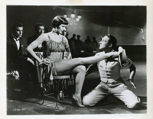 On the set of Singin' in the Rain (1952). Cyd Charisse posed with leg out, Gene Kelly's hat placed on her foot. Gene Kelly kneels to Charisse.