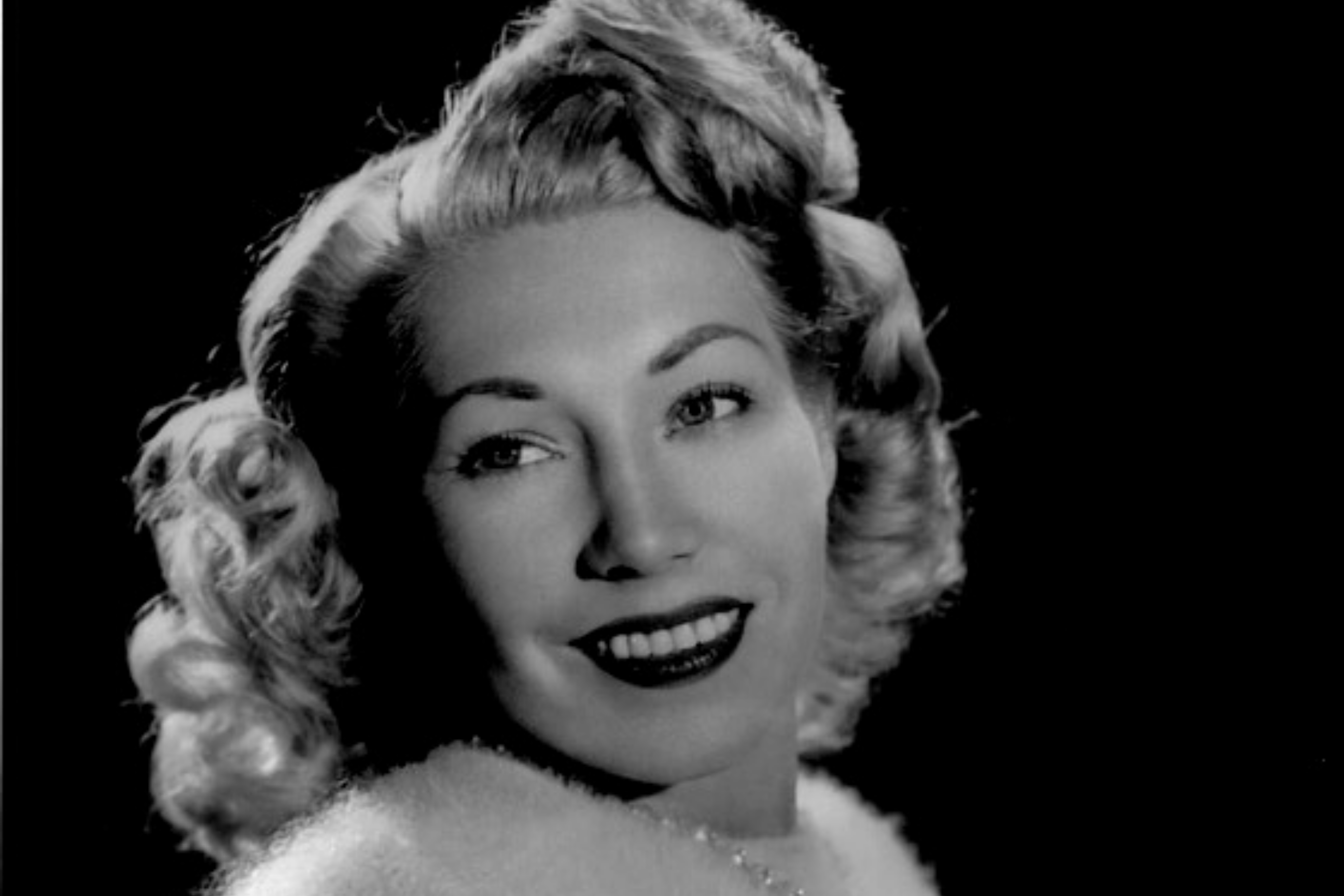 Dolores Fuller smiles and looks to the left. Her blonde hair is coiffed in a 40s style.