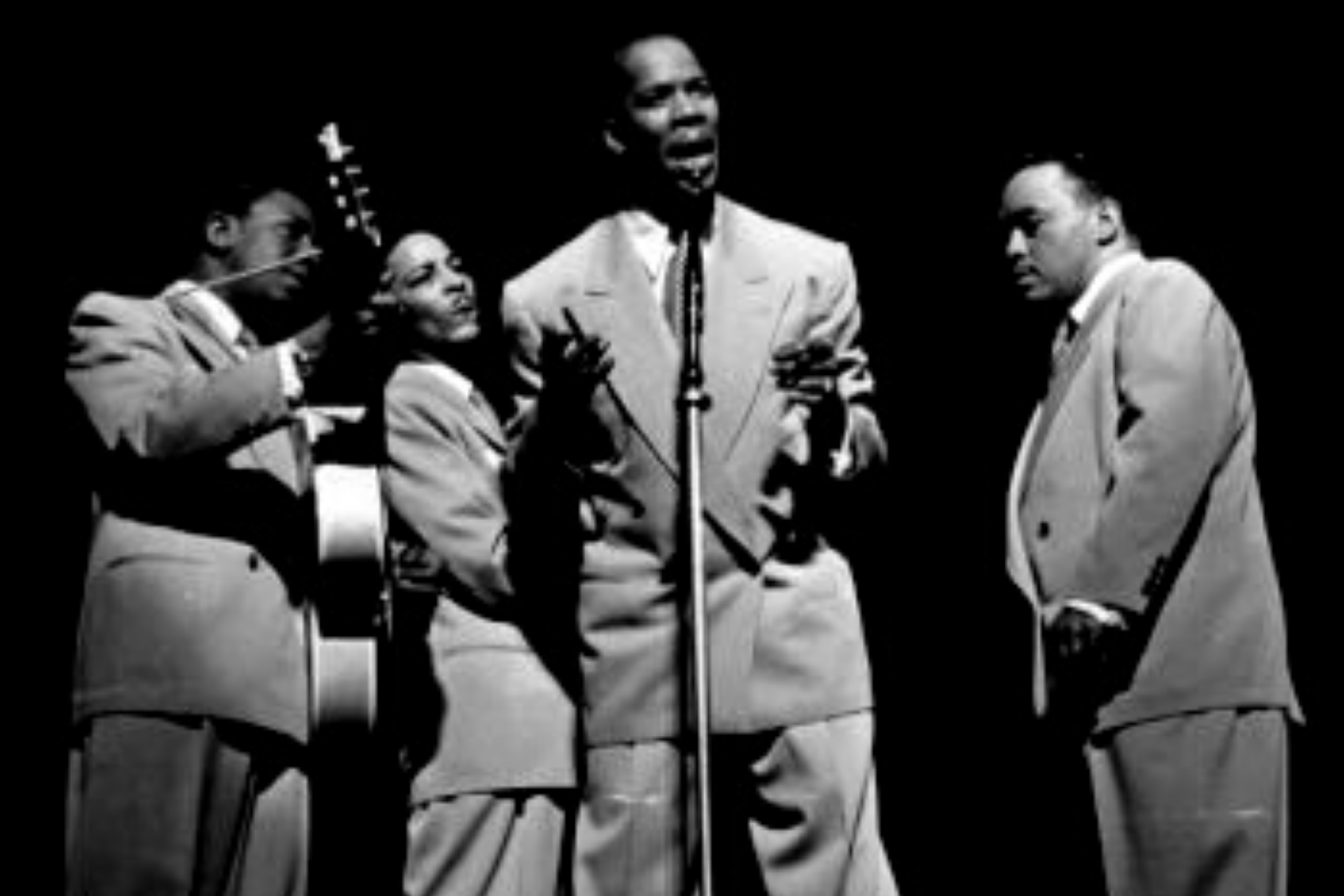The Ink Spots perform around a single microphone in four-part harmony.