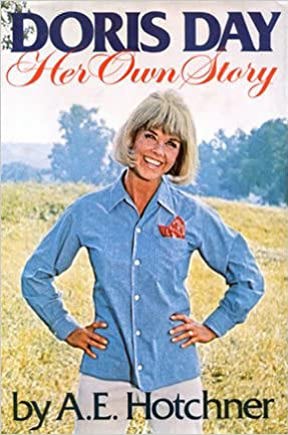 Doris Day: Her Own Story. Doris stands with her hands on her hips in a field and smiles with her head cocked.