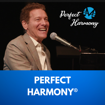 Perfect Harmony. Singer Michael Feinstein sits at a piano and smiles as he sings to an audience.