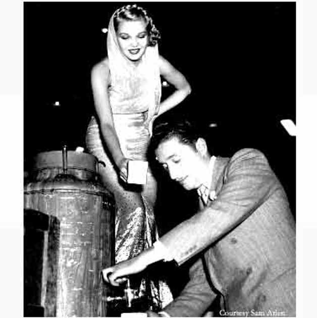 A young Harold Arlen pours water into a cup for the glamorous Tanya Taranda who holds her cup to him.